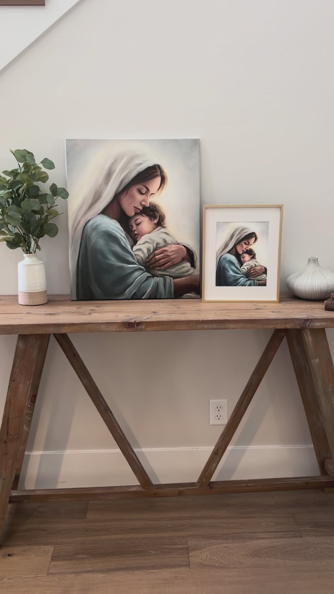 Video of the original painting of Mary holding little Christ next to a small 8x10 print copy in a golden frame sitting next to it. On a wooden entry table. 